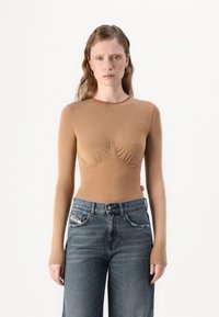 Langärmliges, tailliertes braunes Top mit Raffung am Dekolleté, Rundhalsausschnitt und nahtlosen Bündchen, kombiniert mit hochgeschnittenen blauen Jeans.