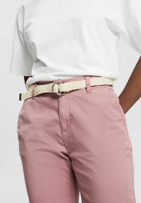 Touwriem in crèmekleur met een metalen zilveren ring, gedragen over lichtroze broek met een ontspannen pasvorm en zijzakken. Witte t-shirt erboven.