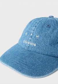 Τζιν μπλε καπέλο baseball με λευκή κεντημένη επιγραφή "CPH STUDIOS" στο μπροστινό μέρος, εμφανιζόμενο σε λευκό φόντο.