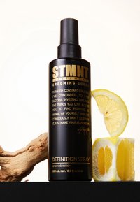 Svart sprayflaska med guldfärgade bokstäver, texturerad yta och matt finish. Intill ligger skivade citroner och en bit drivved.