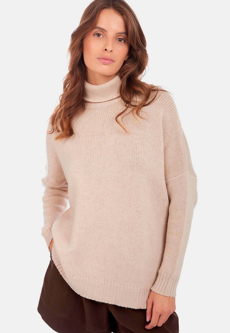Pull à col roulé beige clair avec une coupe décontractée, tricot texturé, manches longues et ourlet côtelé. Porté par-dessus un short marron foncé.