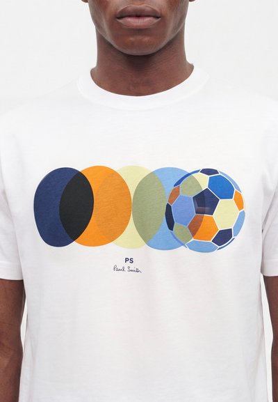Άνδρας που φοράει λευκό T-shirt με πολύχρωμους επικαλυπτόμενους κύκλους και πολύχρωμο γραφικό ποδοσφαιρικής μπάλας, υπογεγραμμένο από PS Paul Smith.