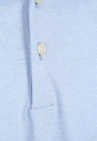 Lichtblauwe polo shirt van gestructureerde stof, met een drieknoopssluiting en contrasterende knopen.