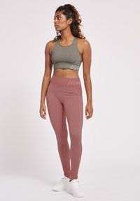 Sportbehå i olivgrön med ribbad textur, parat med högmidjade mauve leggings som har subtil ribbning och logotyp. Vita snörskor fullbordar looken.