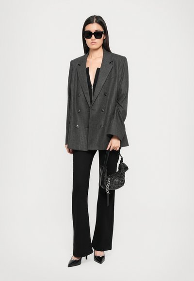 Blazer grigio doppiopetto con righe, abbinato a pantaloni lunghi neri e décolleté a punta. Tiene una piccola borsa nera con borchie.