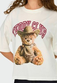 Biała, oversize koszulka z nadrukiem niedźwiedzia w kapeluszu kowbojskim oraz napisem "Teddy Club" w bordowym kolorze nad grafiką. Wykonana z miękkiego materiału bawełnianego.