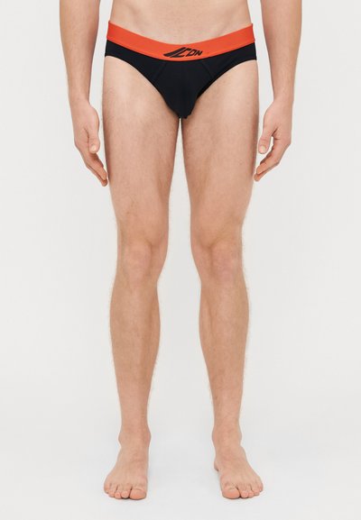 Boxers noirs avec une ceinture rouge, arborant un logo à l'avant. Tissu lisse, coupe ajustée et design à couverture minimale.