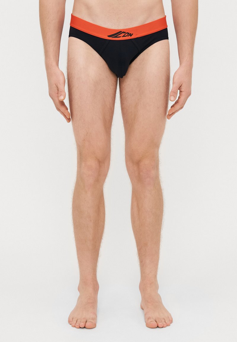 Μαύρα μποξεράκια με κόκκινη ζώνη μέσης, με λογότυπο στο μπροστινό μέρος. Λείος ύφασμα, στενή εφαρμογή και σχεδίαση ελάχιστης κάλυψης.