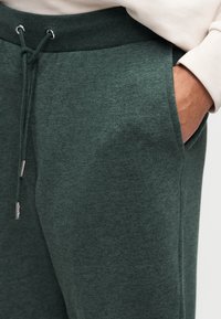 Πράσινα παντελόνια τζόγκινγκ από μείγμα βαμβακιού με ελαστική μέση και κορδόνι, πλαϊνές τσέπες και μαλακή, υφασμένη υφή. Περιλαμβάνονται ασημένιες λεπτομέρειες hardware.