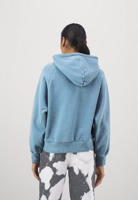 Felpa blu chiaro in pile con cordino sul cappuccio, polsini e vita a coste. Indossata con jeans grigi e bianchi a tonalità marmorizzata.