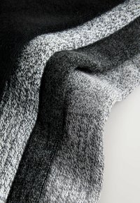 Strikket stof, der viser gradient nuancer af sort og grå med varierende teksturer; glatte og let chunky vævninger blander sig harmonisk.