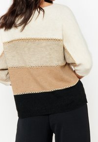 Sweter dziany z poziomymi paskami w kolorach kremowym, beżowym, jasno-brązowym i czarnym. Posiada detale z otwartym ściegiem oraz luźny krój z okrągłym dekoltem.