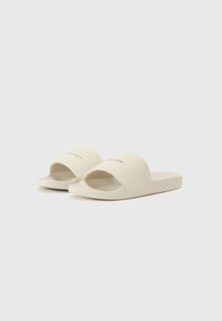 Beige glide sandaler med åpen tå og slip-on-design. Laget av glatt materiale med flat såle og subtil logo på den øvre stroppen.