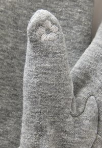 Mittens grigi in maglia con una texture morbida, caratterizzati da un dettaglio floreale ricamato sulla punta e una forma accogliente e arrotondata.