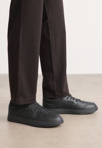 Sorte sneakers med en glat læderlignende overflade, rund tå og snørebåndsdesign. Sammen med mørke, afslappede bukser. Flad gummisål.