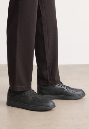 Svarta sneakers med en slät läderliknande yta, rund tå och snörning. I kombination med mörka byxor med avslappnad passform. Platt gummisula.