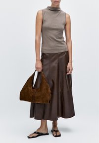 Bruine mouwloze coltrui, gecombineerd met een bruine leren midi-rok en een bruine suède handtas, aangevuld met zwarte sandaaltjes met banden.