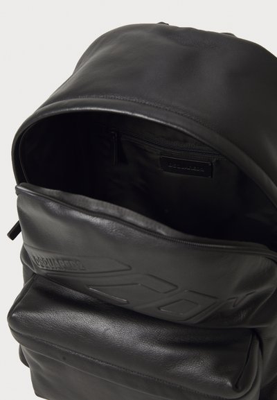 Black leather backpack with smooth texture, large opening, inner zip pocket, and embossed logo detail on the front.