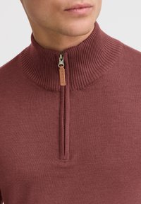 Pull en maille zippé bordeaux avec un col côtelé et un zip en cuir beige portant le texte « BLEND. » Texture lisse et design ajusté.