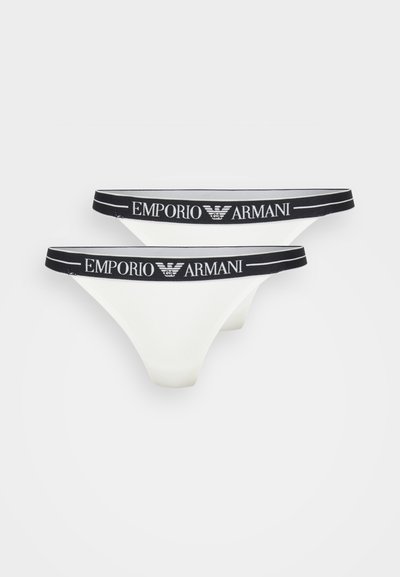 Un slip string blanc avec une taille élastique noire portant le logo "Emporio Armani" en blanc. Matériau lisse, design minimaliste.