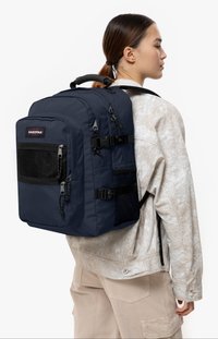 Marinblå Eastpak ryggsäck med en strukturerad design, flera zipplåsfack, nätinslag och justerbara remmar. Texturerad tyg.