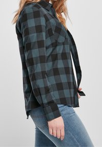 Schwarzes und dunkelteal kariertes Flanellhemd mit Button-Down-Kragen und einer einzelnen Brusttasche, kombiniert mit hellblauen Jeans.