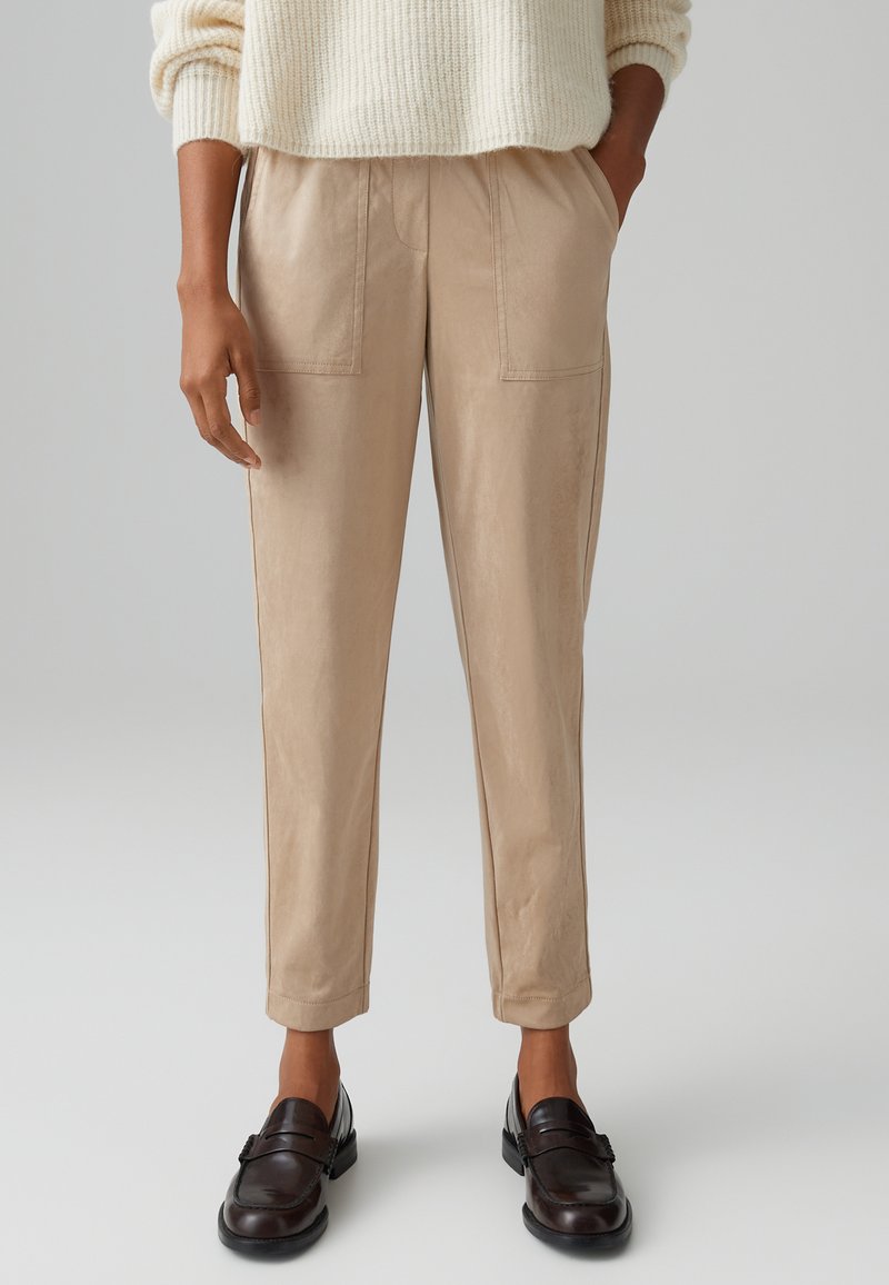 Beige, tapered trousers with two front pockets, elastic waistband, and smooth texture, paired with brown loafers.