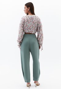 Bloemenprint cropped blouse met zwierige mouwen en strikdetails, gecombineerd met hoge, wijde mintgroene broeken. De schoenen zijn beige met bandjes.