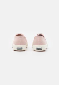 Paire de baskets en toile rose clair vues de dos avec semelles blanches en caoutchouc et logo « SUPERGA » sur les languettes du talon.