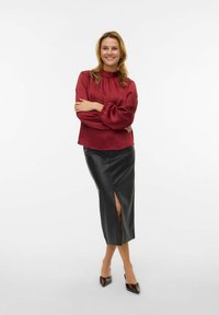 Rode satijnen blouse met geplooide halslijn en volumineuze mouwen, gecombineerd met een nauwsluitende zwarte leren rok met een voorste split.