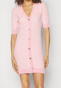 Abito a maglia rosa con maniche corte e scollatura a V, tessuto texturizzato e cinque bottoni argentati sul davanti. Polsini e orlo a costine.