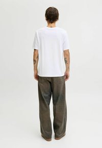 Witte katoenen T-shirt met een klassieke ronde hals, gecombineerd met losse, versleten bruine spijkerbroeken en bruine schoenen.