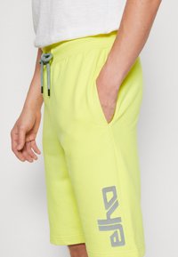 Helle gelbe Shorts aus einem Baumwoll-Mix mit Seitentaschen und einem Kordelzugbund. Graues Logo auf dem linken Bein gedruckt.