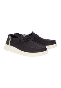 Scarpe in tela nera testurizzata con suole intrecciate bianche, lacci e un distintivo dettaglio di cucitura laterale. Occhielli rinforzati e accenti con logo.
