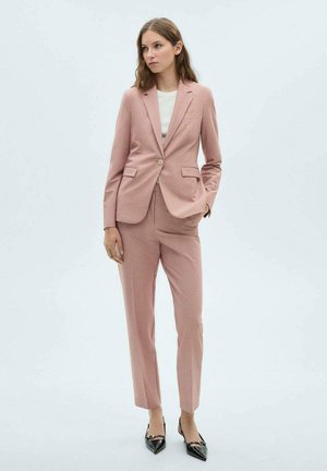 Light pink tailored suit with a single-button blazer and straight-fit trousers. Features side pockets and smooth texture. Black pointed heels.