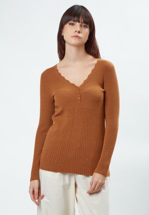Pull marron à manches longues avec un col en V festonné et des boutons. Texture douce avec des éclats subtils. Associé à un pantalon clair.