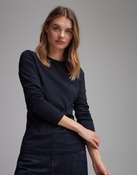 Navy long-sleeve t-shirt in soft fabric with round neckline and fitted design. Model wearing it has arms crossed, with jeans visible below.