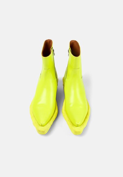 Neon gula läderankelstövlar med spetsig tå och en texturerad gul sula. Har sidodragkedjor och en slät ovansida.