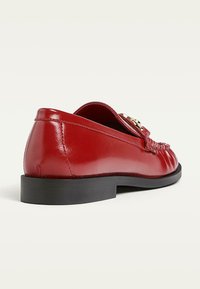 Red leather loafer with a smooth finish, low black sole, decorative stitched detail, and a gold-tone accent on the side.