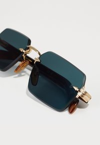 Ochelari de soare pătrați cu lentile de culoare verde închis, rame negre, detalii aurii și accente de țestoasă la tâmple.