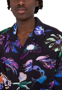 Camisa de manga corta de tela negra con patrones florales multicolores. Incluye un bolsillo en el pecho y cuello abotonado.