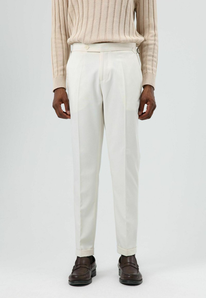 Witte, op maat gemaakte broek met een gladde textuur, voorzien van een slim fit, plooien en een knoopsluiting, gecombineerd met bruine loafers.