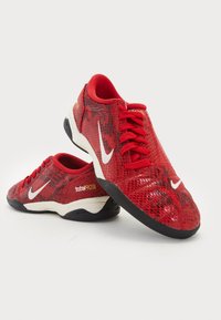 Röda syntetiska sportskor med ett ormskinnsmönster, med vita Nike-loggor, svarta sula och tydlig logotypdetalj på hälen.