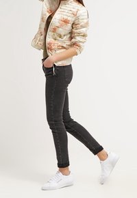 Padded kovová bunda s květinovým vzorem v krémových a zlatých tónech; doplněná tmavými úzkými džínami a bílými teniskami.