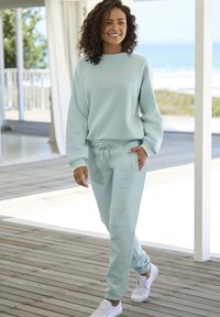 Felpa azzurro chiaro e pantaloni jogger abbinati realizzati in tessuto morbidissimo. Presentano un cordino regolabile e un logo ricamato. Indossati con sneakers bianche.