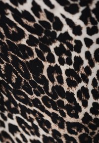 Luipaardprint stof met grote zwarte vlekken op een beige achtergrond, met een gladde textuur en een lichte glans.