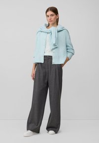 Hellblaues gestricktes Cardigan mit Knopfverschluss, kombiniert mit grauen Faltenhosen und weißen Sneakers. Cardigan lässig über die Schultern gelegt.