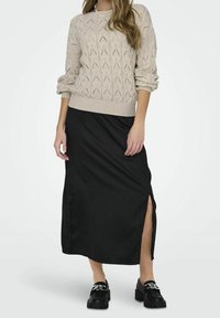 Beżowy sweter dziany z diamentowymi wzorami, czarna satynowa spódnica maxi z bocznym rozcięciem i solidne czarne loafersy z srebrnymi akcentami.