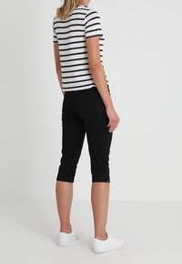 Randig t-shirt med kort ärm i beige och marin, tillsammans med svarta capribyxor. Vita sneakers synliga. Enkelt, avslappnat plagg.