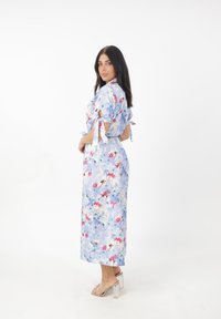 Bloemrijke jurk in lichtblauw met roze en paarse accenten. Heeft korte mouwen met strikjes en een vloeiende silhouet, gemaakt van lichtgewicht stof.